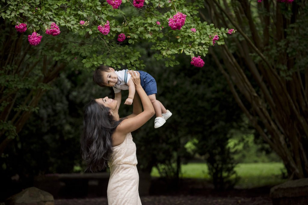Morven Park in Loudoun County. Mother in pink rent the runway dress holds baby boy up in the air with blooming pink crape myrtles in the background