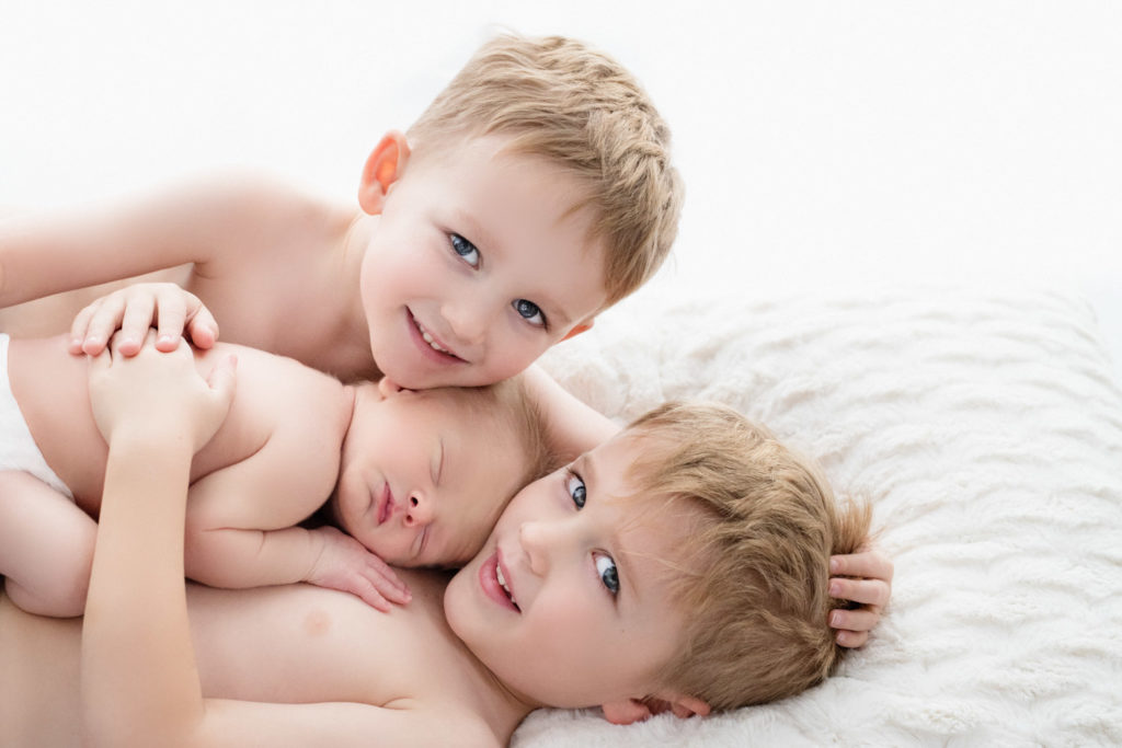 Caucasian brothers hold their newborn baby brother and smile looking at the camera