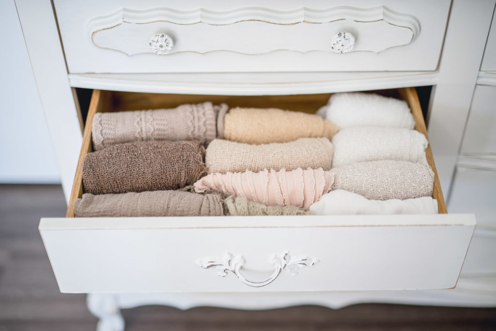An open drawer in a vintage white dresser displays neutral toned newborn wraps at a photography studio in leesburg virginia