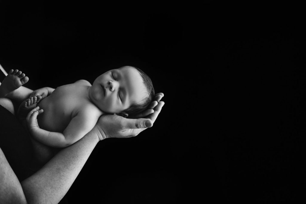 black and white image of a caucasian baby boy sleeps in dad's hands