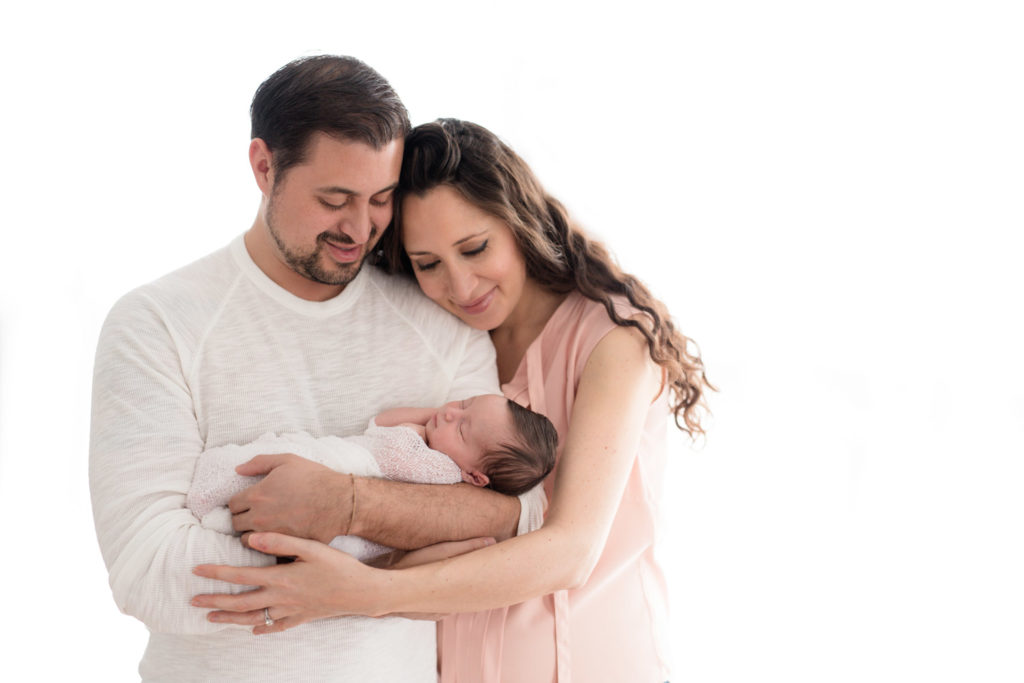 Persian family with dad dressed in white linen top and mom dressed in silk blush and pink flowing top holding baby girl