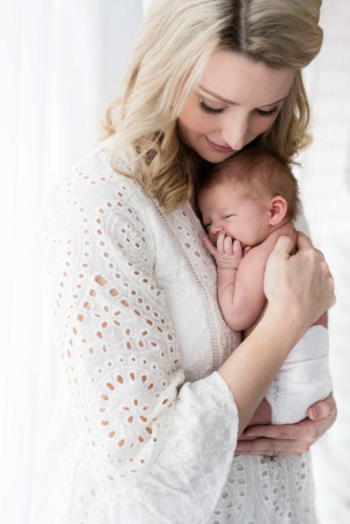 Caucasian mom with blond hair dressed in textured white eyelet top holding her baby boy