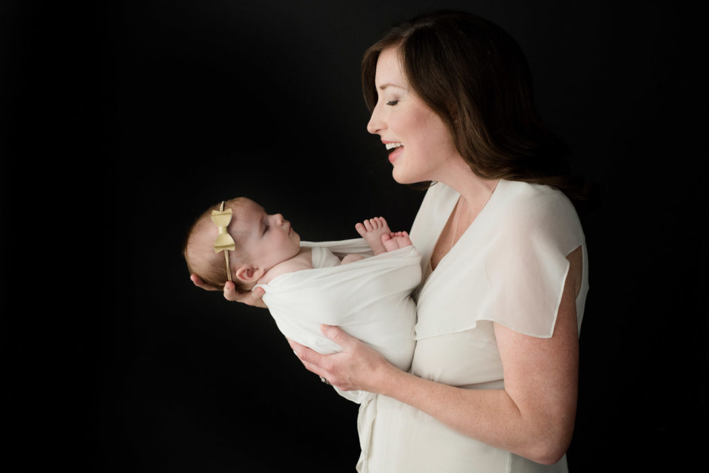 Caucasian mom dressed in silk cream top holding her newborn baby girl