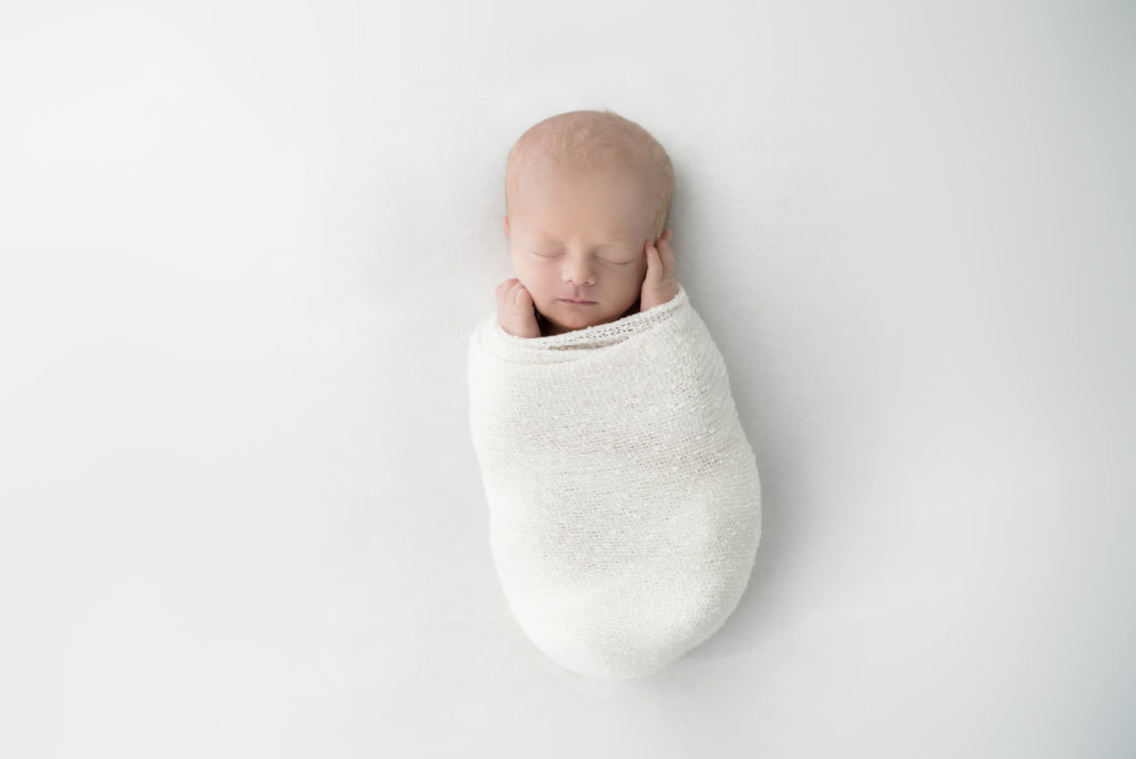 newborn baby boy on white blanket in white wrap