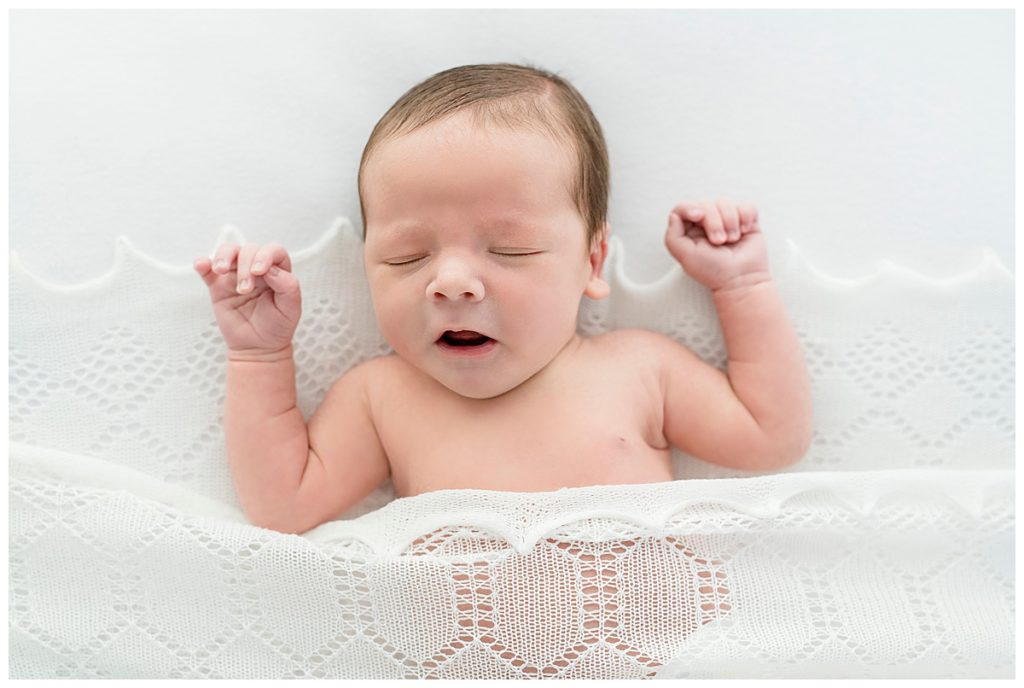 sleeping baby boy on white blanket yawning and stretching arms