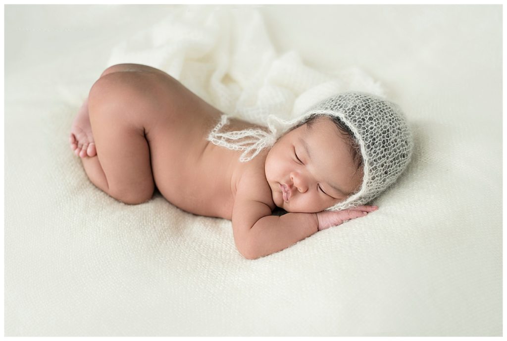 sleeping baby girl on white blanket with white knit hat