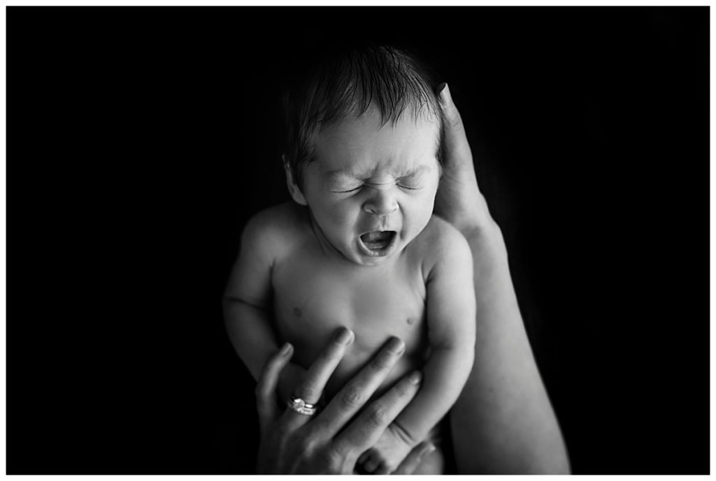 black and white studio image of newborn yawning in mom's arms