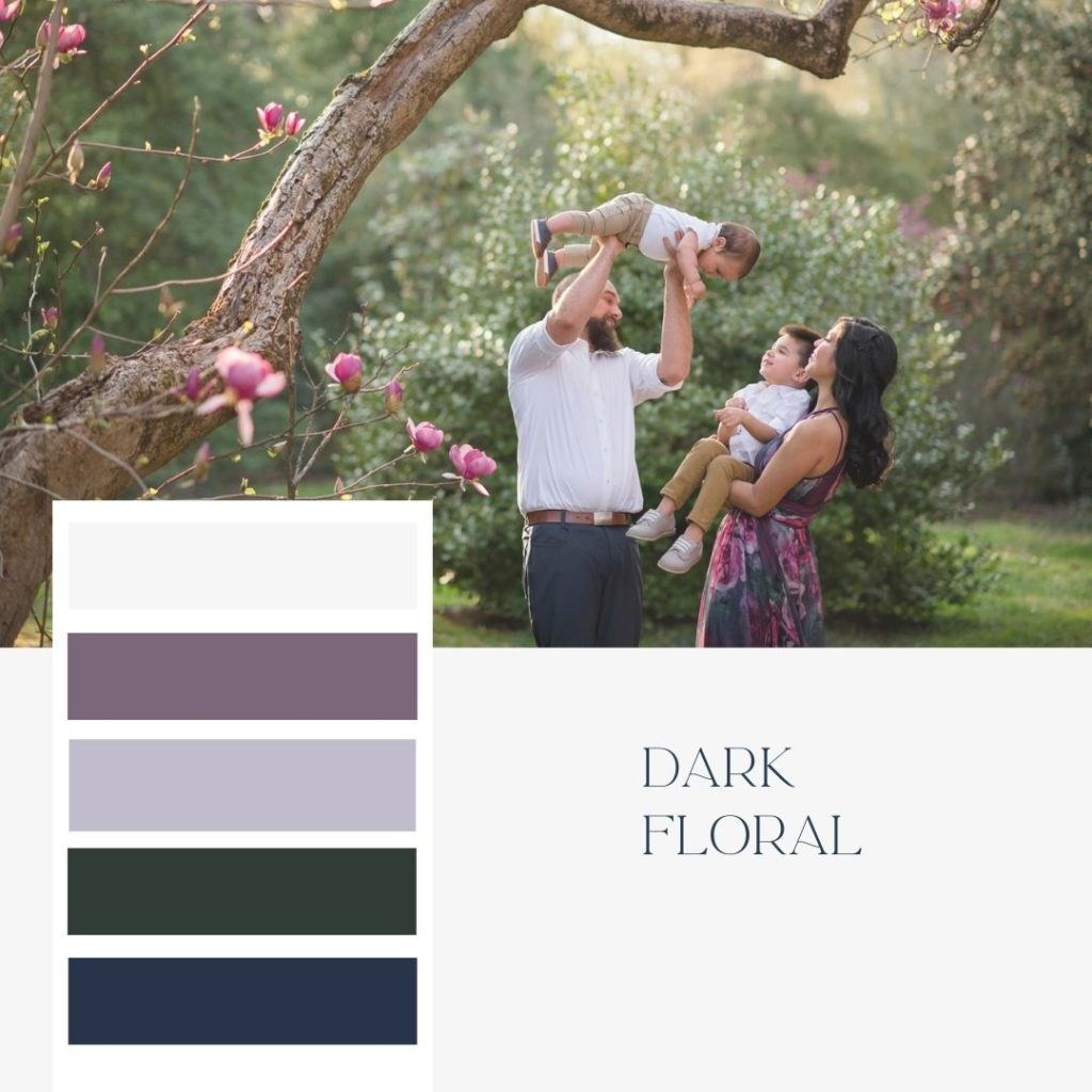 Mom and dad with two young boys posing for family photo under dogwood tree in springtime. Dark floral color schemes for family photos with purple, dark green, and navy blue