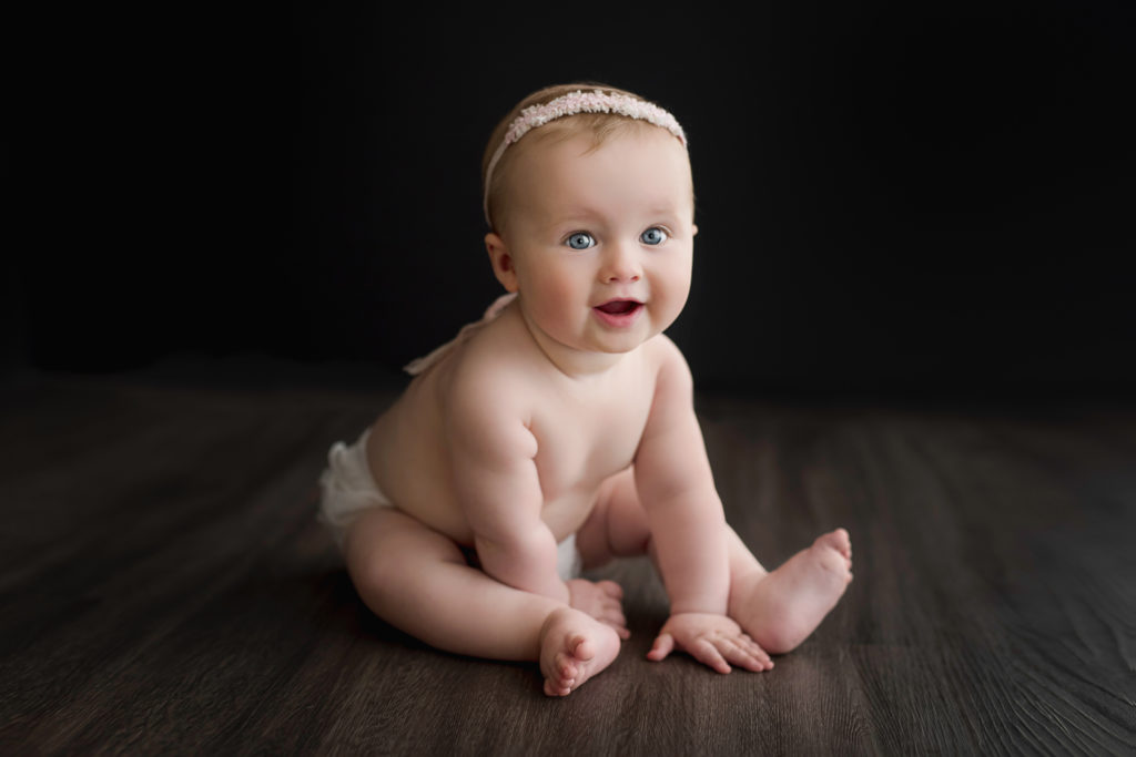 6-month-old baby girl sitting and smiling for professional photo.