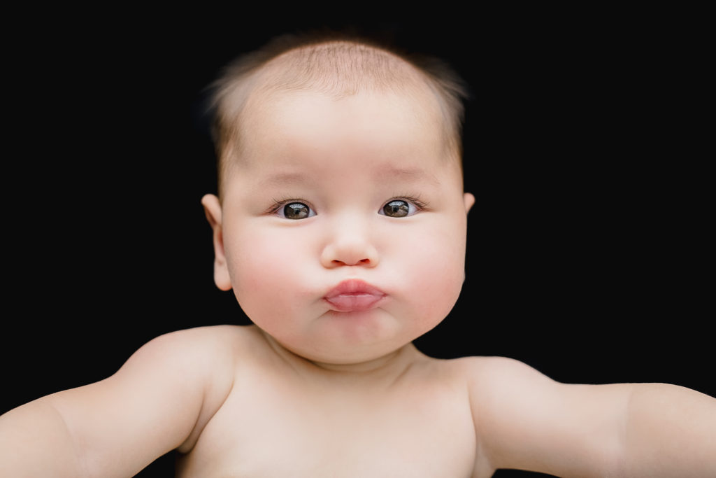 Baby looking at camera and pursing lips in professional photo with black background.