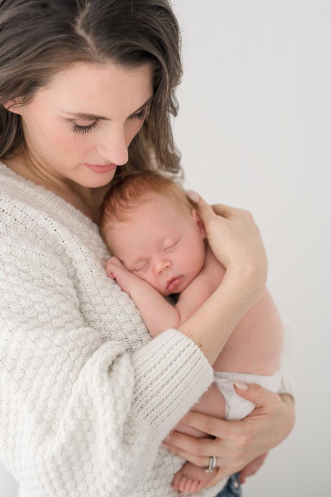 Alt text mom in soft glam makeup holds newborn in photo studio in Leesburg