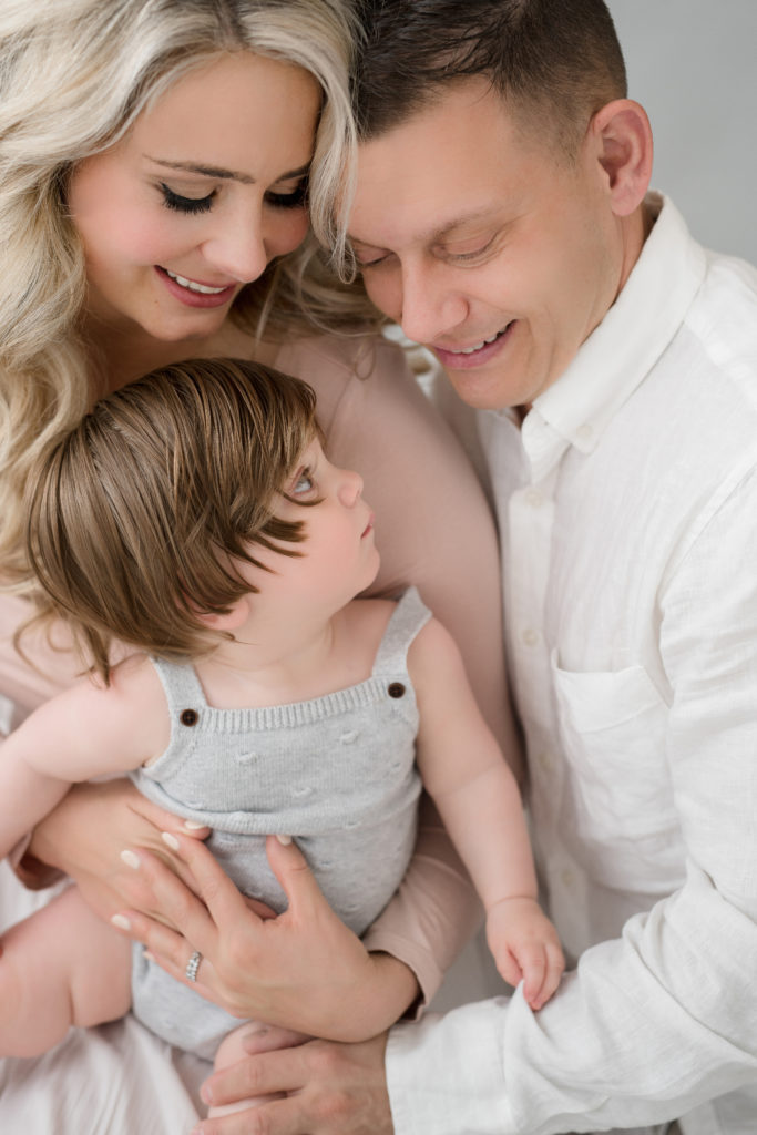 A mom, dad, and baby snuggle together in a portrait studio in Leesburg