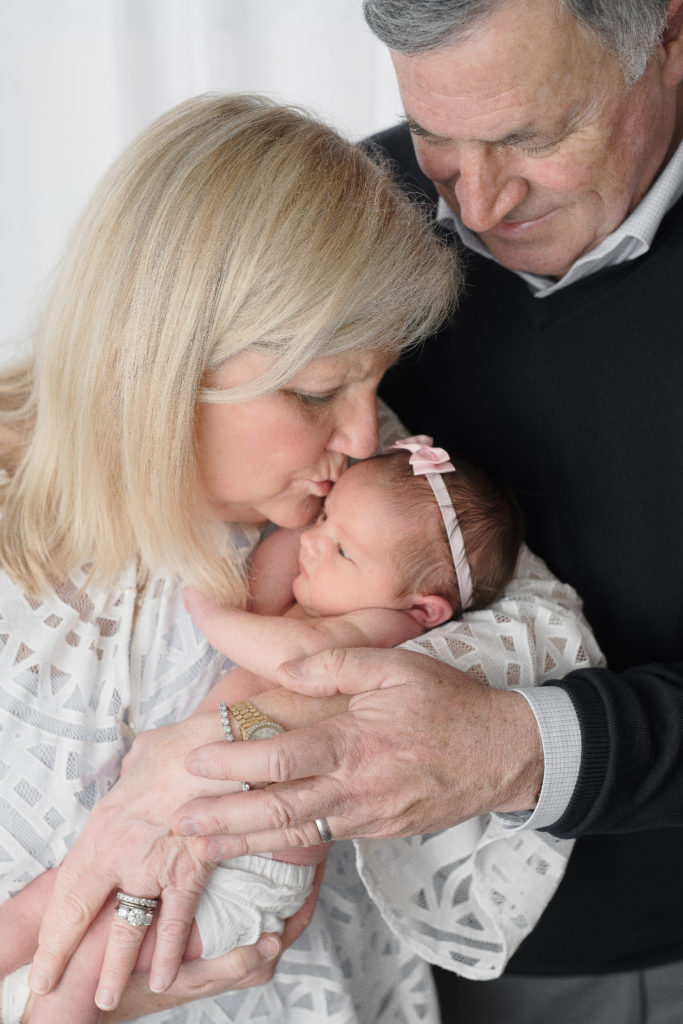 Grandparents hug and kiss newborn baby