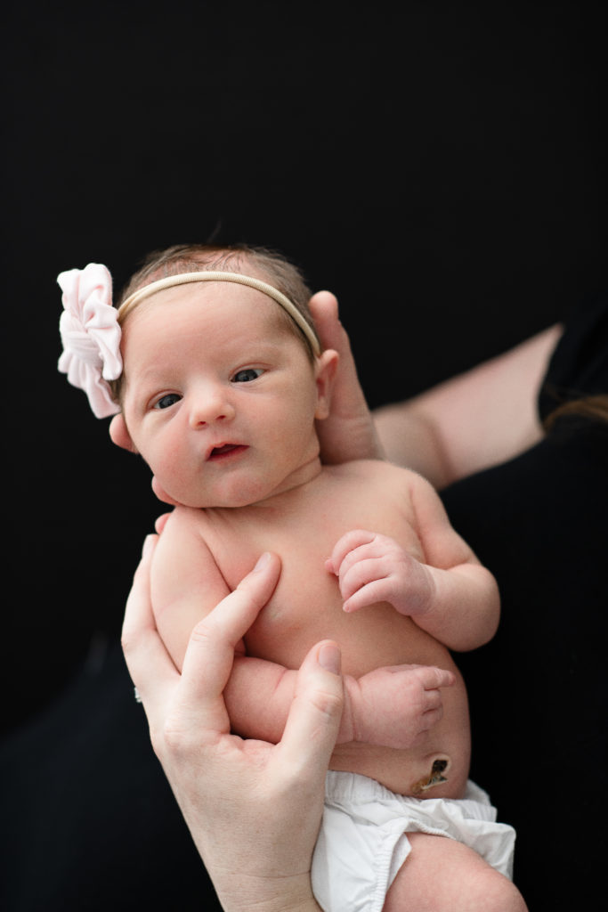 newborn baby girl with bow on in front of a black background
