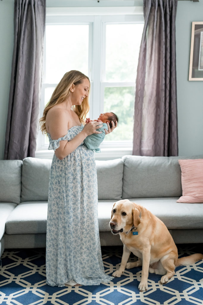 Mom holds her newborn in her home with their dog nearby 