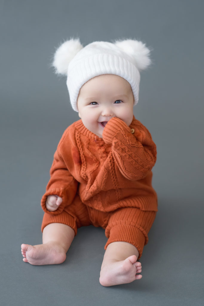 baby with hat with two pom poms looks at camera during baby photo session