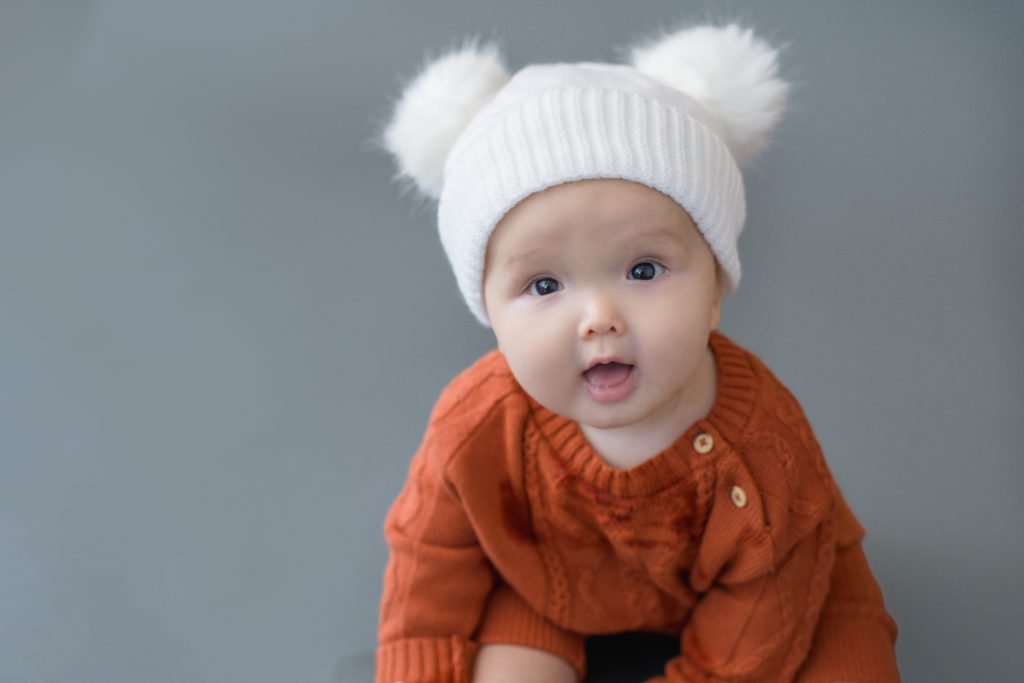 baby with hat with two pom poms looks at camera during baby photo session